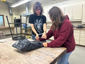Two people working on a corpse in a trash bag prop