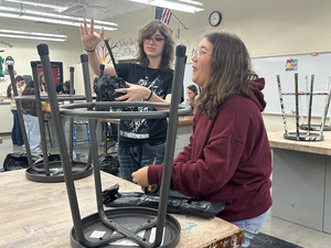 Two people working on a corpse in a trash bag prop.